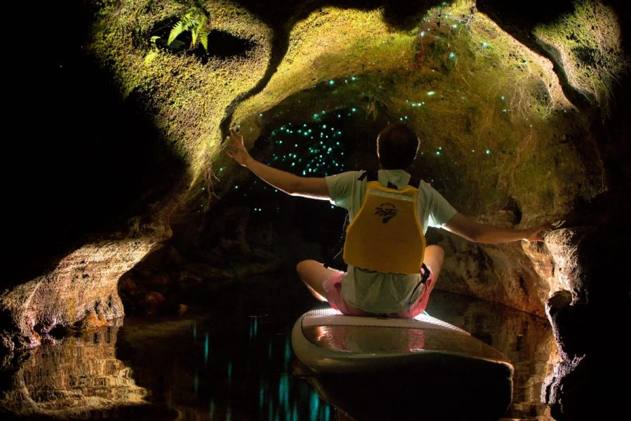 A man riding a small floating board inside a cave with glow worms.