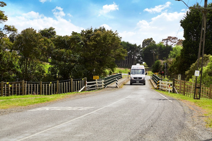 A white campervan crossing a small bridge in Orere Point.