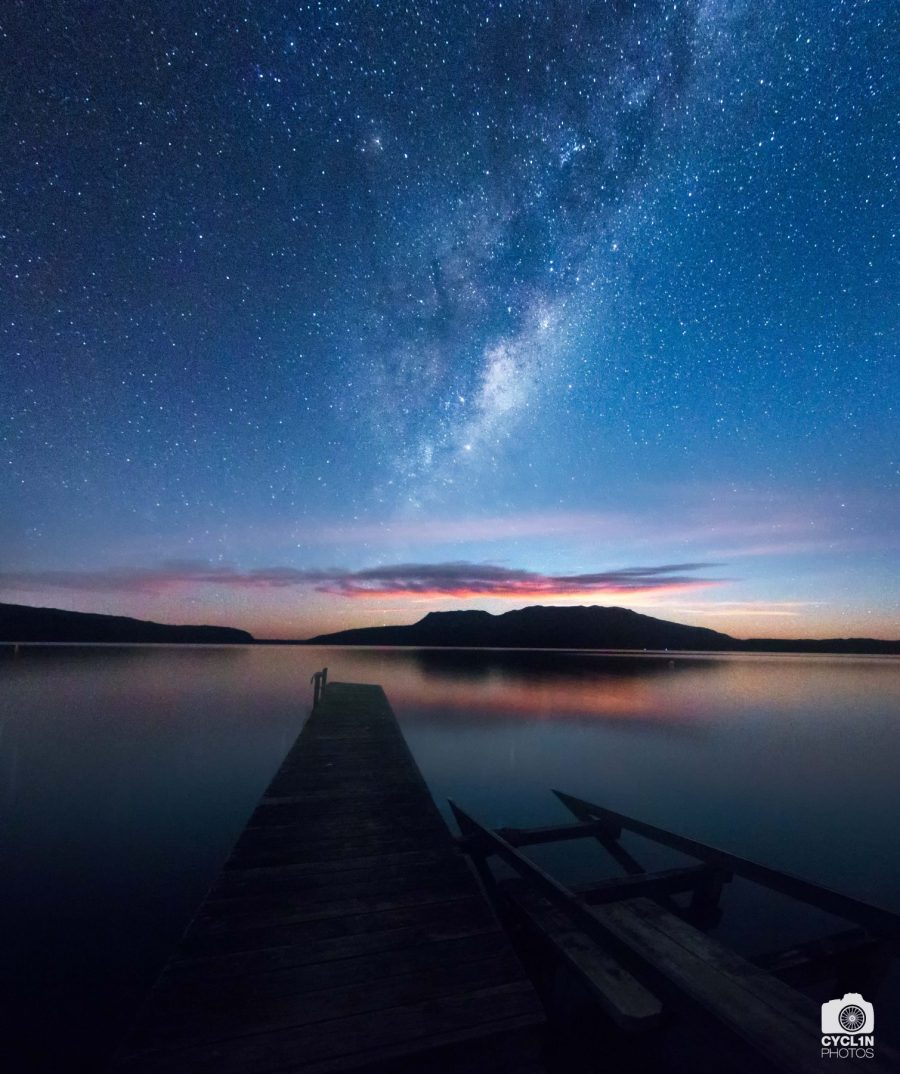 A pontoon stretching on a calm lake with a view of the stars and Milky Way seen on a cloudless sky.