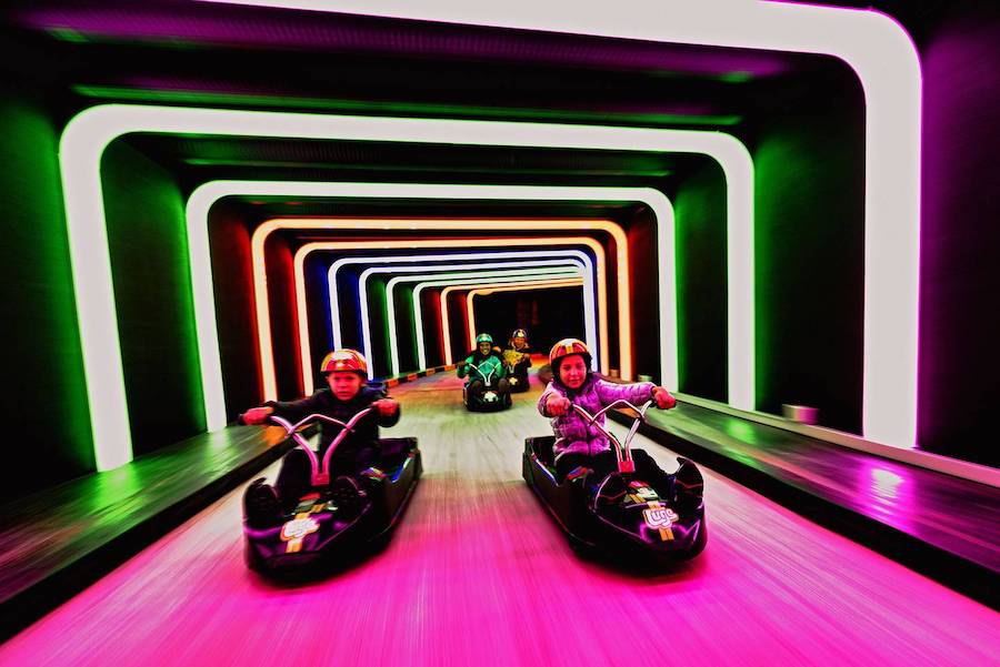 Kids in luge rides with neon lighting while inside a tunnel.